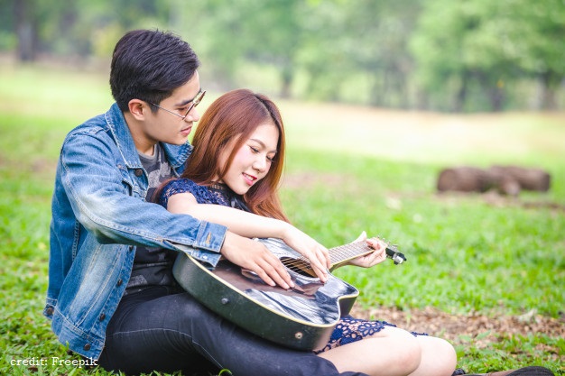 asian-couple-love-playing-acoustic-song-guitar-sitting-grass-park_39730-855